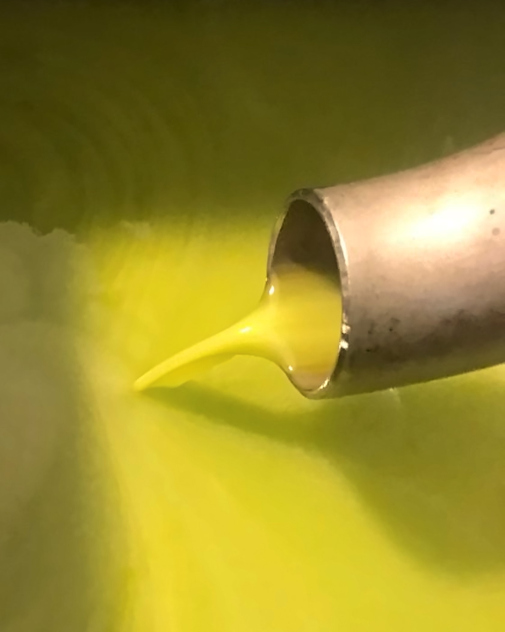 Thick green-gold new olive oil pouring from the steel spout of the press into the tank